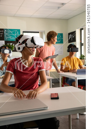 Diverse classmates wearing vr headsets using laptops while teacher with tablet in classroom Diverse classmates wearing vr headsets using laptops while teacher with tablet in classroom 141540785