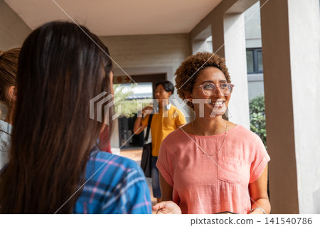 Diverse friends chatting and walking through campus walkway with smartphone, headphones Diverse friends chatting and walking through campus walkway with smartphone, headphones 141540786