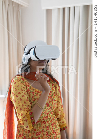 Indian woman wearing yellow kurta exploring virtual world with vr headset at home Indian woman wearing yellow kurta exploring virtual world with vr headset at home 141540855