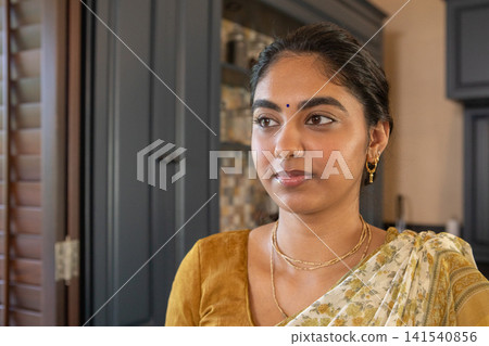 Indian woman standing in kitchen, in mustard blouse and saree by gray cabinets, tile backsplash Indian woman standing in kitchen, in mustard blouse and saree by gray cabinets, tile backsplash 141540856