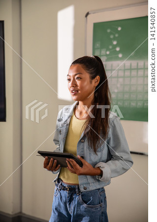 Asian woman presenting in classroom holding tablet with diagrams and light patch Asian woman presenting in classroom holding tablet with diagrams and light patch 141540857