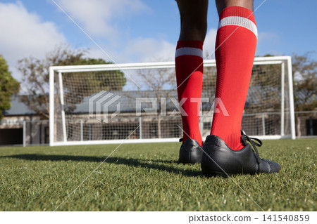 African American man standing on grass pitch facing goal wearing red socks and cleats, copy space African American man standing on grass pitch facing goal wearing red socks and cleats, copy space 141540859