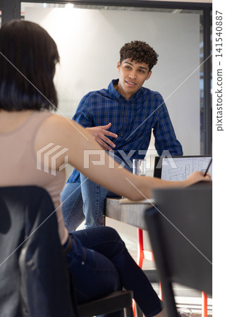 Diverse coworkers discussing laptop sketches at conference table in modern office with water glass Diverse coworkers discussing laptop sketches at conference table in modern office with water glass 141540887