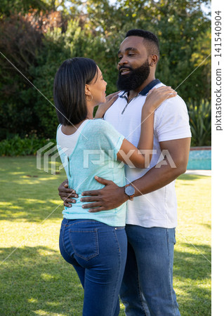 Asian and African American couple holding each other in backyard garden with visible wristwatch Asian and African American couple holding each other in backyard garden with visible wristwatch 141540904