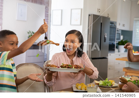 African American mother and son passing roasted chicken drumsticks around dining table in kitchen African American mother and son passing roasted chicken drumsticks around dining table in kitchen 141540905