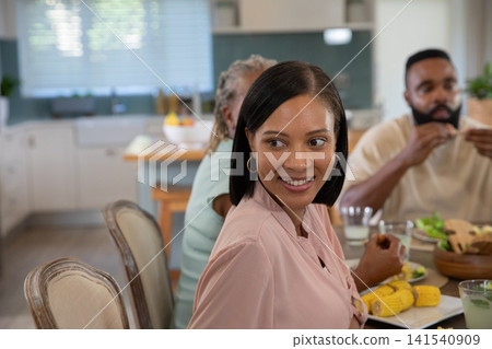 Diverse family sharing meal around wooden dining table in modern kitchen with salad bowl and corn Diverse family sharing meal around wooden dining table in modern kitchen with salad bowl and corn 141540909