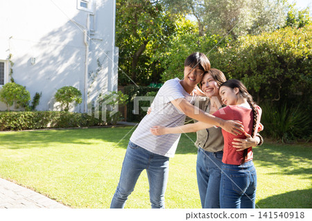 Asian family sharing warm hug on manicured lawn beside air conditioning unit and paved walkway Asian family sharing warm hug on manicured lawn beside air conditioning unit and paved walkway 141540918