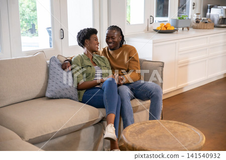 African american couple sitting on couch holding hands in living area with bowl of oranges African american couple sitting on couch holding hands in living area with bowl of oranges 141540932