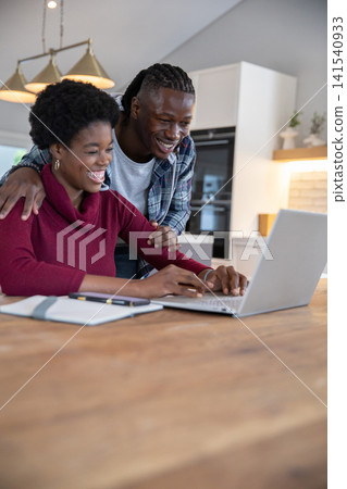 African american couple working on silver laptop and notebook at kitchen table under lights African american couple working on silver laptop and notebook at kitchen table under lights 141540933