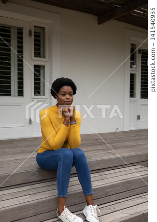 African american woman sitting on front porch step under pergola pondering with shuttered doors African american woman sitting on front porch step under pergola pondering with shuttered doors 141540935