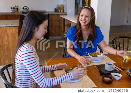 Asian mother and daughter sharing salad bowls and water glasses at kitchen dining table Asian mother and daughter sharing salad bowls and water glasses at kitchen dining table 141540956