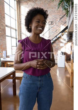 African american woman smiling, standing in office wearing purple top, jeans with pc monitor African american woman smiling, standing in office wearing purple top, jeans with pc monitor 141540993