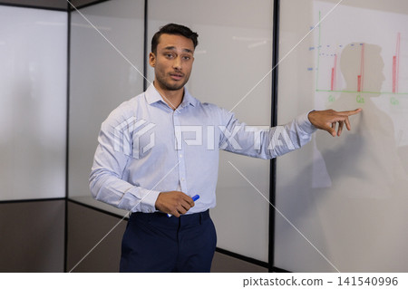 Man standing beside whiteboard pointing at bar chart with blue marker cap in meeting room Man standing beside whiteboard pointing at bar chart with blue marker cap in meeting room 141540996