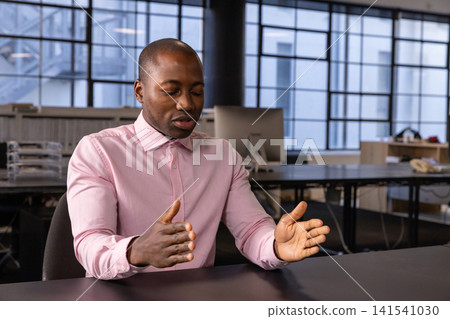 African american man sitting at desk in office gesturing with hands among computer monitors African american man sitting at desk in office gesturing with hands among computer monitors 141541030
