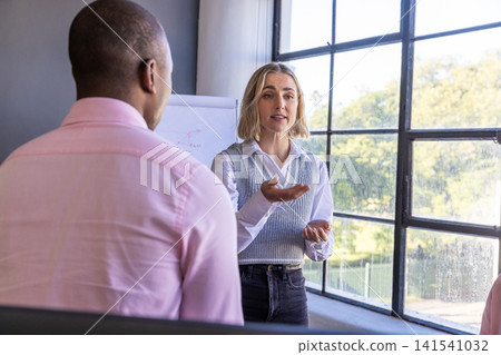 Diverse coworkers presenting ideas in meeting room near window with flipchart Diverse coworkers presenting ideas in meeting room near window with flipchart 141541032