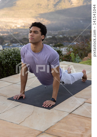 African american man practicing yoga on stone patio with valley view, mat, smartwatch African american man practicing yoga on stone patio with valley view, mat, smartwatch 141541044