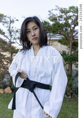 Asian woman adjusting black belt on gi in residential backyard garden in front of house Asian woman adjusting black belt on gi in residential backyard garden in front of house 141541046