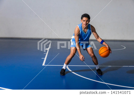African american teenage male basketball player dribbling basketball on court wearing wristband African american teenage male basketball player dribbling basketball on court wearing wristband 141541071