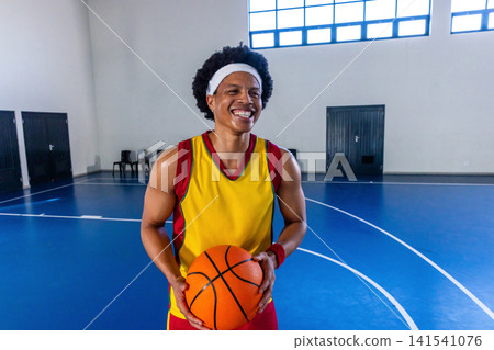 African american man dribbling basketball on blue court wearing yellow red jersey, shorts African american man dribbling basketball on blue court wearing yellow red jersey, shorts 141541076
