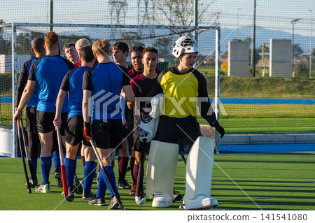 Male field hockey teams shaking hands after match on turf in front of goal net Male field hockey teams shaking hands after match on turf in front of goal net 141541080