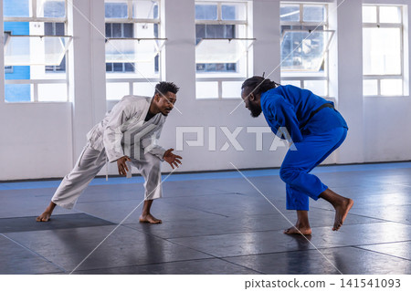 African american male training partners sparring in dojo wearing gi on mats near windows African american male training partners sparring in dojo wearing gi on mats near windows 141541093