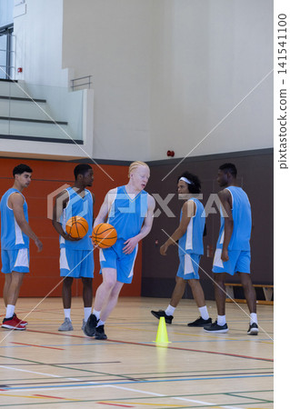 Diverse male basketball team in uniforms holding basketballs by cone, preparing drill on court Diverse male basketball team in uniforms holding basketballs by cone, preparing drill on court 141541100