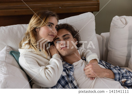 Couple cuddling on white sofa in living room with plush cushions and wooden upright piano Couple cuddling on white sofa in living room with plush cushions and wooden upright piano 141541111