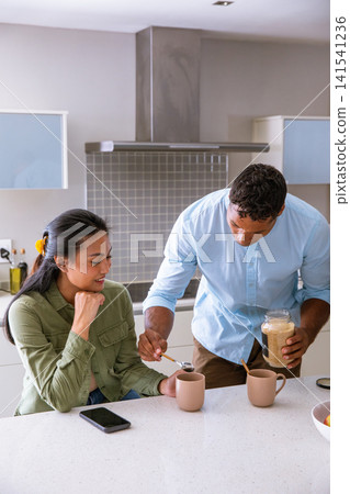 Diverse couple scooping sugar into ribbed ceramic mugs on white quartz countertop in kitchen Diverse couple scooping sugar into ribbed ceramic mugs on white quartz countertop in kitchen 141541236