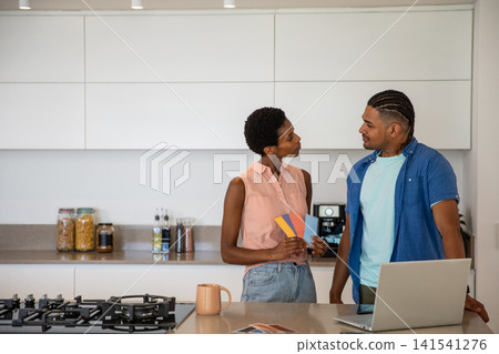 African American couple discussing paint swatch cards at kitchen island with laptop and mug African American couple discussing paint swatch cards at kitchen island with laptop and mug 141541276