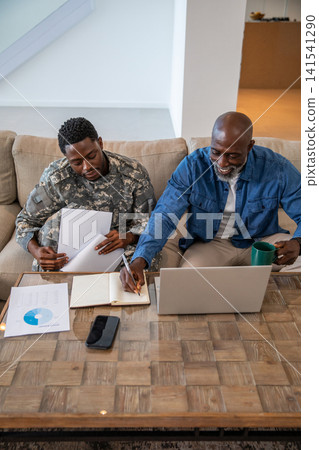 African american father and son reviewing charts with him in camouflage uniform on couch African american father and son reviewing charts with him in camouflage uniform on couch 141541290