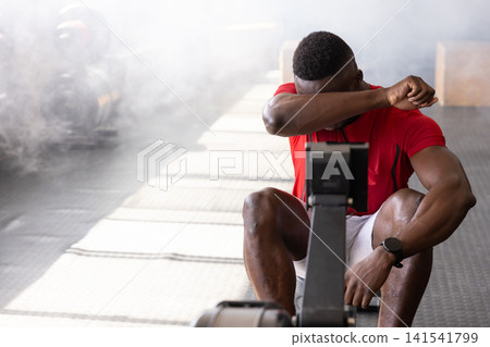 African American man wiping sweat from forehead after rowing on rowing machine inside gym facility African American man wiping sweat from forehead after rowing on rowing machine inside gym facility 141541799