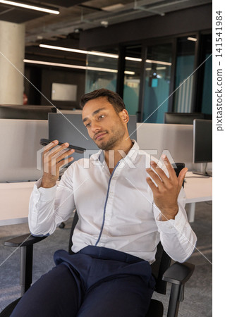 Middle eastern man sitting in swivel chair speaking on smartphone in office with monitors Middle eastern man sitting in swivel chair speaking on smartphone in office with monitors 141541984