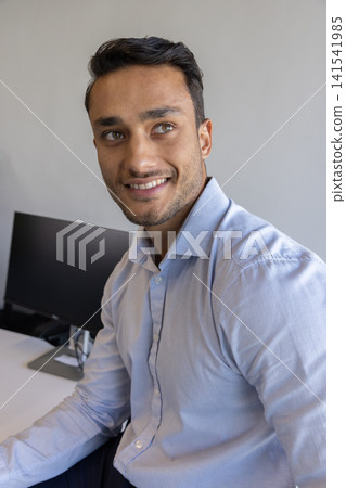 Businessman in blue shirt working on keyboard at white desk with black monitor and mouse Businessman in blue shirt working on keyboard at white desk with black monitor and mouse 141541985
