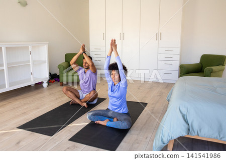 Diverse couple practicing yoga on black mats at home exercise area in workout clothes Diverse couple practicing yoga on black mats at home exercise area in workout clothes 141541986