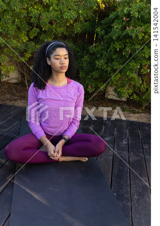 African american woman meditating on yoga mat wearing sportswear, headband, fitness tracker 141542004