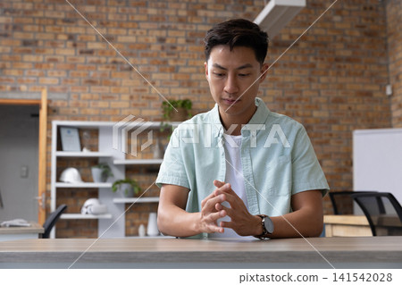 Asian man sitting at wooden table in office meeting space Asian man sitting at wooden table in office meeting space 141542028