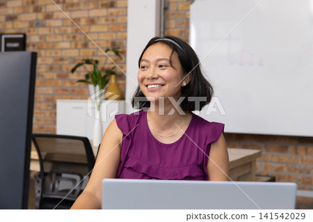 Asian woman looking at monitor with laptop at office with whiteboard behind Asian woman looking at monitor with laptop at office with whiteboard behind 141542029