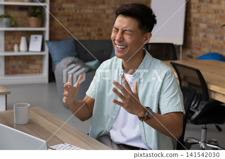 Asian man typing on laptop and wireless keyboard at desk with coffee mug in office Asian man typing on laptop and wireless keyboard at desk with coffee mug in office 141542030
