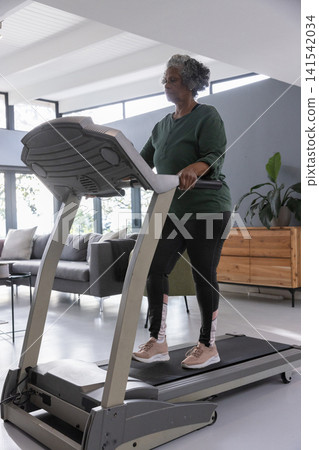 Senior african american woman exercising on treadmill in room with sofa, copy space Senior african american woman exercising on treadmill in room with sofa, copy space 141542034