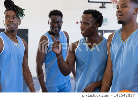 African american male basketball teammates in jerseys planning plays in gym with basketball African american male basketball teammates in jerseys planning plays in gym with basketball 141542037
