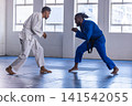 Sparring in dojo, african american men in white and blue gi with belts on mats 141542055