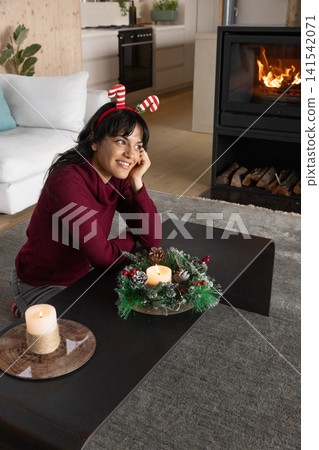 Woman sitting on floor leaning on coffee table with candle wreath in living room near fireplace 141542071