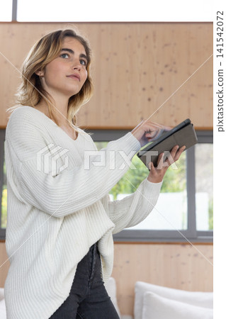 Woman using black tablet device in modern lounge with wood-paneled walls and white cushioned sofa Woman using black tablet device in modern lounge with wood-paneled walls and white cushioned sofa 141542072