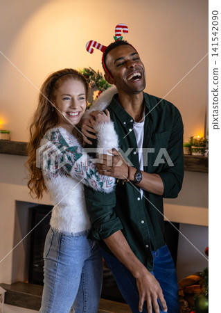 Diverse couple hugging, laughing in decorated living room by fireplace mantel with lit candles Diverse couple hugging, laughing in decorated living room by fireplace mantel with lit candles 141542090