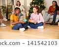 Diverse children wearing antler headbands exchanging gifts on floor at home, christmas tree 141542103