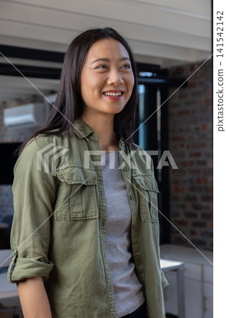 Asian woman standing in office under exposed beams by desk and air conditioner near brick wall Asian woman standing in office under exposed beams by desk and air conditioner near brick wall 141542142