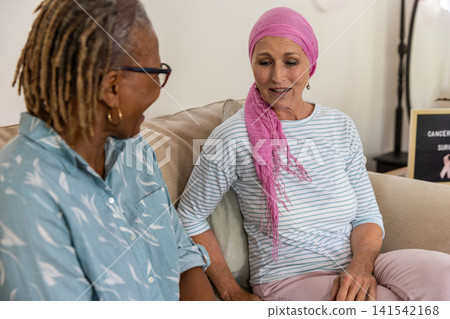 Diverse female friends sitting on sofa conversing at home by cancer survivor letter board 141542168