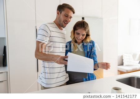 Couple standing at kitchen island reading printed document beside coffee mug and sink faucet 141542177
