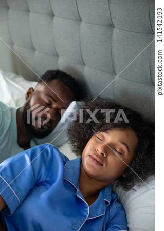 Diverse couple lying side by side sleeping in bedroom with white pillows, gray tufted headboard Diverse couple lying side by side sleeping in bedroom with white pillows, gray tufted headboard 141542193