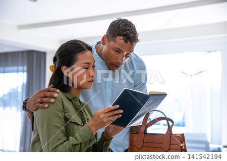 Diverse couple leaning over shoulder examining dark blue notebook next to tan handbag Diverse couple leaning over shoulder examining dark blue notebook next to tan handbag 141542194